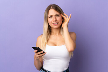 Young blonde woman using mobile phone isolated on purple background unhappy and frustrated with...