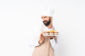 Young man holding muffin cake over isolated white background scheming something