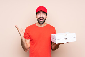 Young man holding a pizza over isolated background with shocked facial expression