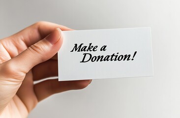 Hand Holding White Card with 'Make a Donation!' Text, Isolated on White Background for Charity and Support Concept
