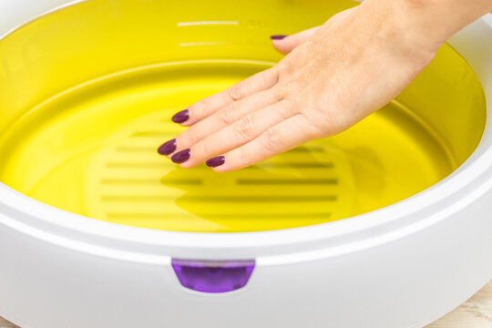 a woman's hand is dipped into melted paraffin. female hand immersed in paraffin bath. woman doing paraffin therapy for hands, close-up. wax machine for paraffin therapy. spa manicure procedure. 