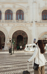 Vlogger traveler woman with suitcase using phone at train station in Lisbon. Business travel and solo tourism concept. Gen Z girl influencer shooting social media stories on the street