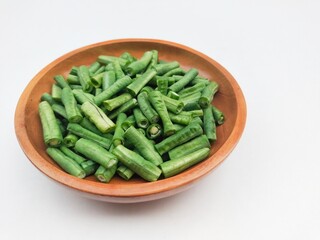 Long beans (Vigna Unguiculata ssp. Sesquipedalis) that have been cut into pieces in a wooden bowl on a white background.