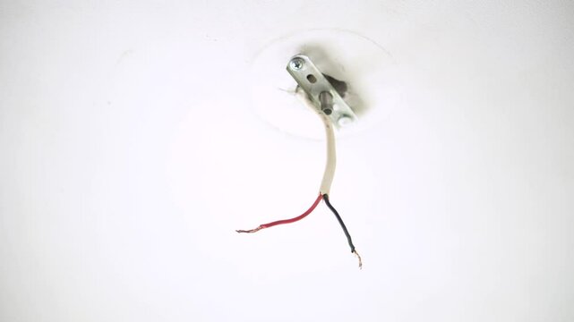 Electrician twists wires in Chandelier on ceiling. Professional worker tightens bolts on ceiling in building closeup