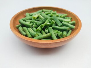 Close-up of long beans (Vigna Unguiculata ssp. Sesquipedalis) that have been cut into pieces in a wooden bowl on a white background. High angle view. 