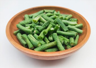 Close-up of long beans (Vigna Unguiculata ssp. Sesquipedalis) that have been cut into pieces in a wooden bowl on a white background. High angle view. 