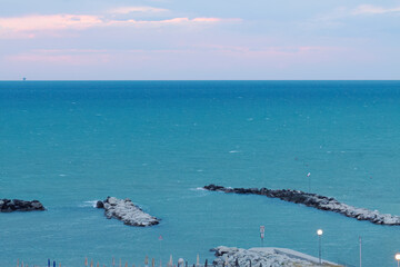 Fototapeta premium blue sea and pink sky during a storm, stormy sea, blue sea, purple sky, azure blue, empty sandy beach during a storm, breakwater and high waves, splashing waves