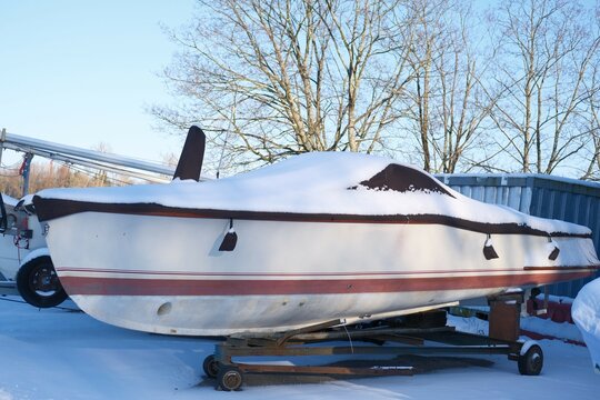 White motor boat or launch on boat trailer during winter storage at yacht club, covered with tarpaulin awning on sunny winter day. Warehouse on the boat pier or parking outdoors