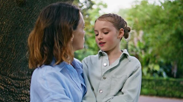 Gentle mother talking daughter touching her nose with finger at park closeup