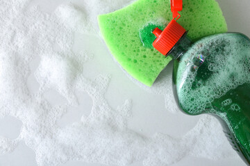 Open detergent bottle spilling detergent onto a green scouring pad
