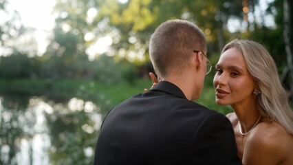Fototapeta premium Newlywed bride and groom sharing tender moments near riverside, expressing deep emotional connection amid lush green landscape during golden hour sunlight