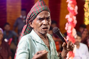 Senior rural artist performing in a program with microphone in hand 