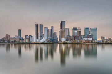 Fototapeta premium Canary Wharf shot from the Greenwich peninsula at slack tide in the golden hour, creating a lovely reflection in the water and a pastel coloured sky.
