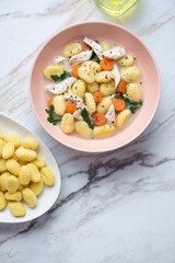 Roseate bowl with creamy chicken gnocchi soup, vertical shot on a white stone background with space, above view