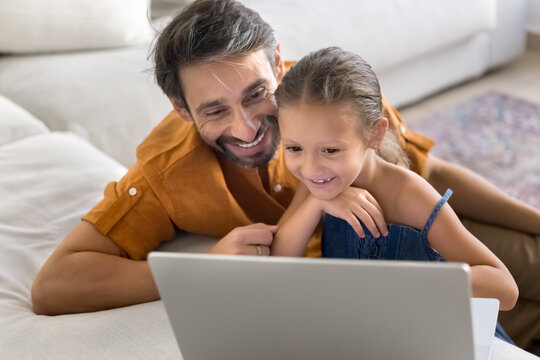 Interested Portuguese mature man and his little 5s cute daughter exploring new educational platform, learning amusing AI program or chatting using modern laptop. Family enjoy internet usage on leisure