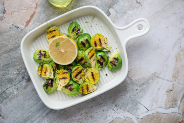 Beige serving tray with grilled Brussels sprouts, horizontal shot on a grey granite background, view from above