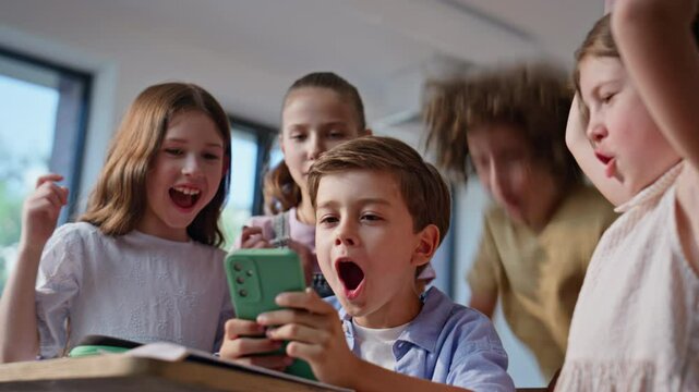 Excited schoolchildren playing mobile phone having fun together in class closeup