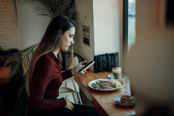 Chica joven con pelo largo tomando café y tortitas en cafetería estilo cozy