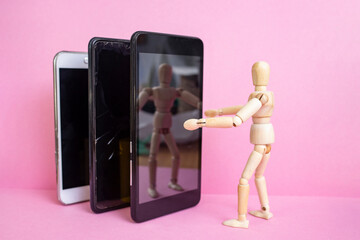 Wooden mannequin embracing three smartphones on pink background, taking a selfie miniature concept