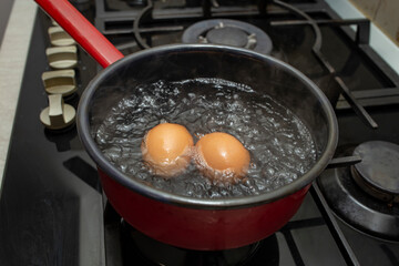 Two orange eggs boiling in a  black pot with bubbles and steam, soft focus  close up