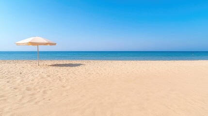 Fototapeta premium A single sun umbrella stands on a quiet sandy beach by the calm blue ocean during a bright sunny day.