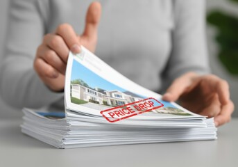Person reviewing real estate brochures with price drop stamp on modern homes