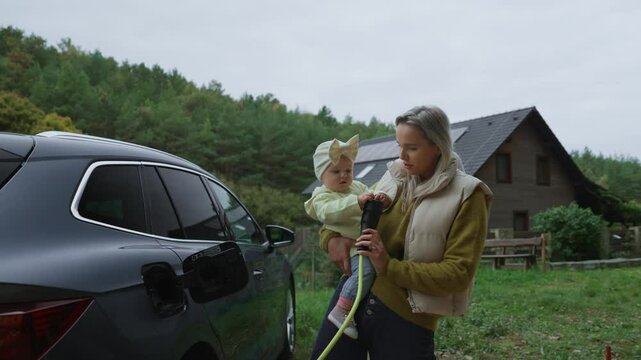 Young mom and girl charging family electric car. EV home charging station.