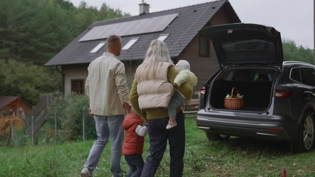 Rear view of family walking to their electric car parked in front of house. House with rooftop solar panels and own EV home charging station.