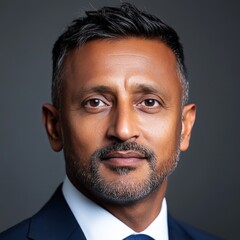 Fototapeta premium Mature businessman with salt and pepper beard and deep gaze wearing dark suit standing confidently against dark grey background in executive branding portrait for corporate leadership marketing