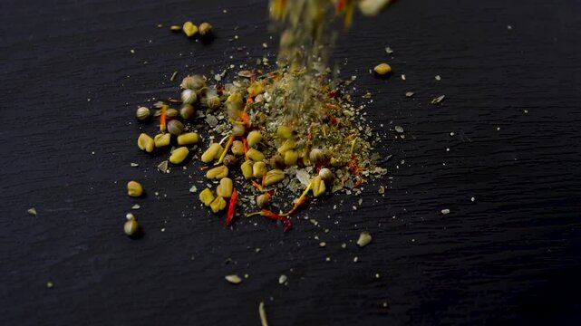 Green and yellow mixture of dried herbs and spices falling on dark textured surface: coriander, basil, dill, bay leaf, saffron, fenugreek 