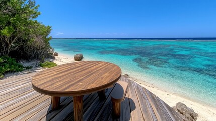 Obraz premium Round wooden table on a deck overlooking a turquoise ocean and sandy beach. Lush green foliage is visible in the foreground. Bright sunny day