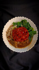 Chicken Noodle Soup with Chili Paste and Vegetables
A top-down view of a bowl of chicken noodle soup with chili paste and green vegetables, served on a white plate against a dark background 'mie ayam'