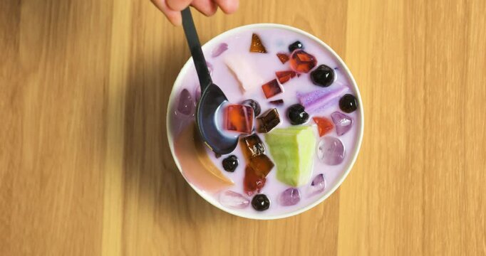 Vibrant taro milk dessert swirling with colorful jelly, creamy pudding base combining smooth texture and sweet visual appeal while mixing with ice cubes