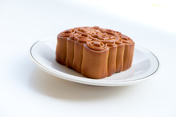 Mooncake on a white plate with silver rim, side-angle shot. Bright lighting shows texture and detail of the crust.
