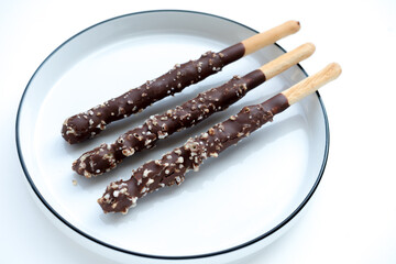Overhead view of chocolate-covered bread sticks with nuts on a white plate. Bright, even lighting. Flat lay food photography