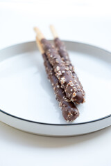 Chocolate-dipped biscuit sticks with nut pieces on a white plate. Soft light highlights the textures. Appetizing snack photo