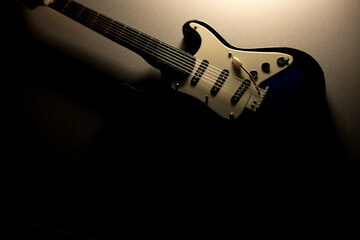Display electric guitar on dark surface. Decorative model, dramatic lighting. Shadow and light, music theme. Studio shot, moody.