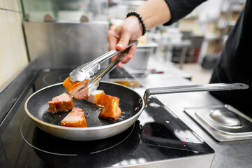 A chef skillfully sears pieces of meat in a frying pan, showcasing a professional kitchen environment with modern cooking equipment.