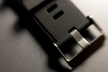 Watch band buckle close-up. Metal clasp, dark rubber strap. Macro detail, timekeeping accessory. Modern design, textured surface.