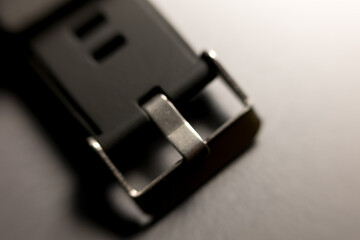 Watch band buckle close-up. Metal clasp, dark rubber strap. Macro detail, timekeeping accessory. Modern design, textured surface.