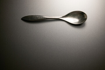 Spoon on gray surface. Metal utensil, simple shot. Top-down view, neutral background. Clean, minimalist composition.