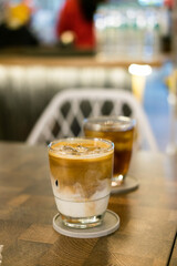 Hot latte & iced tea on cafe table. Layered coffee, cool iced beverage, indoor setting, warm drink, refreshment.