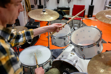 Drummer with drumsticks playing drum set in music studio. 