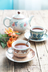 A beautiful ceramic cups and saucers with tea on a old wooden table with tea pot. Selective focus.