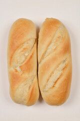 A top-down shot of two plain white bread rolls with diagonal cuts, placed side by side on a light background