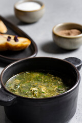 Soup with green sorrel in black ceramic pot on gray background