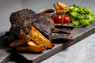 grilled pork ribs with french fries and vegetables on a wooden board