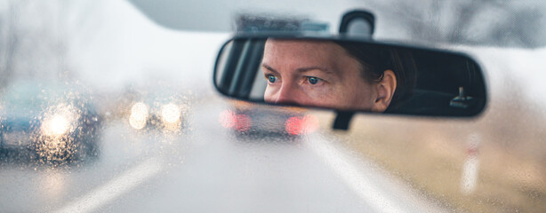 Female driver face at car rear view mirror on a rainy day