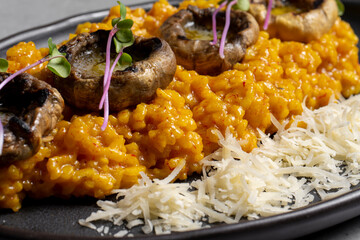 Pumpkin risotto with mushrooms and parmesan cheese on black plate