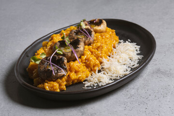 Pumpkin risotto with mushrooms and parmesan cheese on black plate